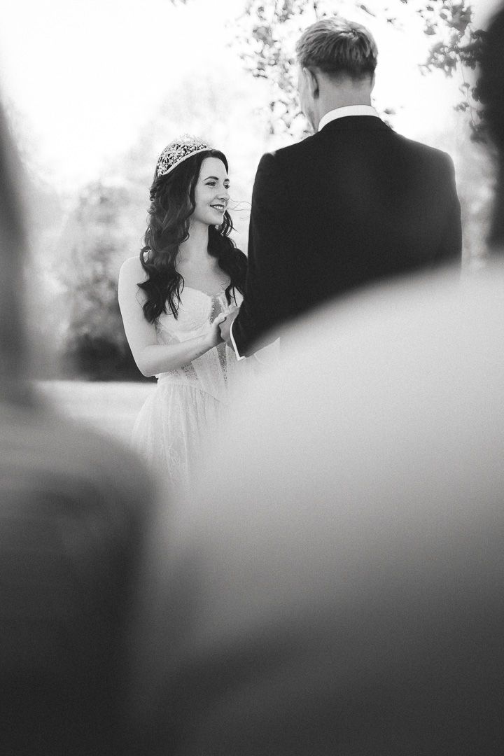 Black and white wedding portrait showing bride in white gown with tiara looking lovingly at groom in dark suit outdoors.