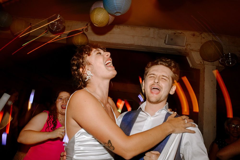 Wedding party dancing and celebrating in a dimly lit reception venue with warm ambient lighting.