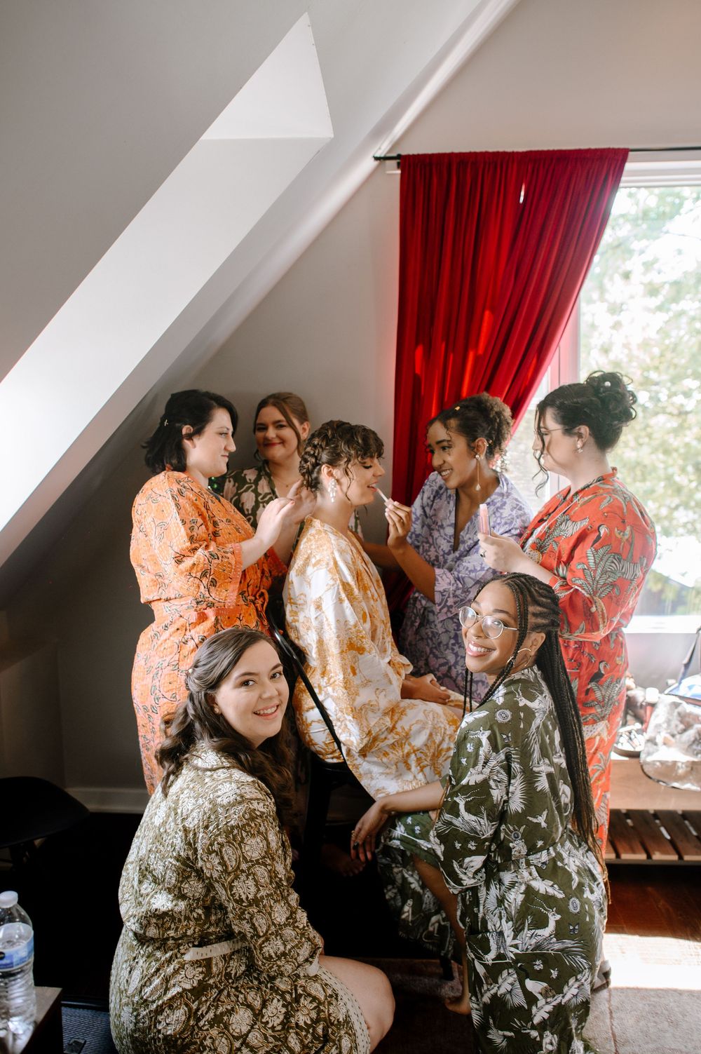 Wedding party getting ready in a bright room with red curtains and candid moments of celebration.