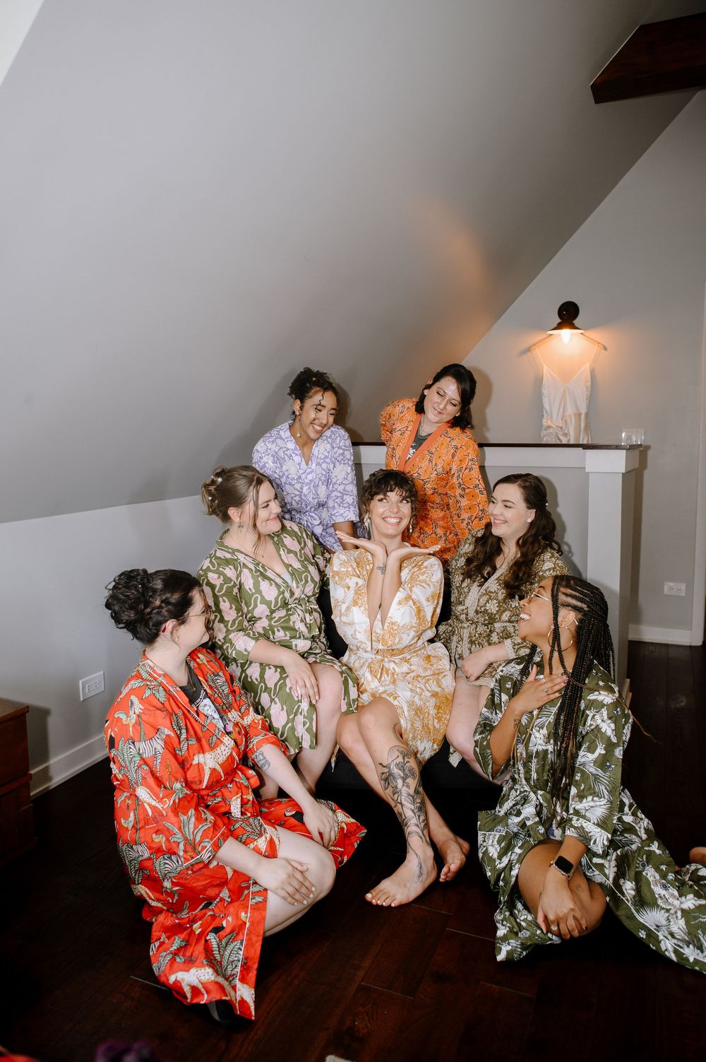 A group poses together wearing colorful floral robes and lounging in an attic room with hardwood floors and a wall lamp.
