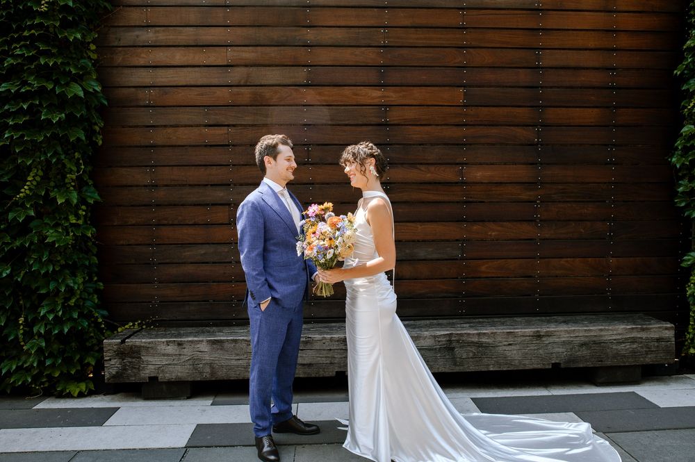 Wedding couple in elegant attire posing against rustic wooden wall backdrop.