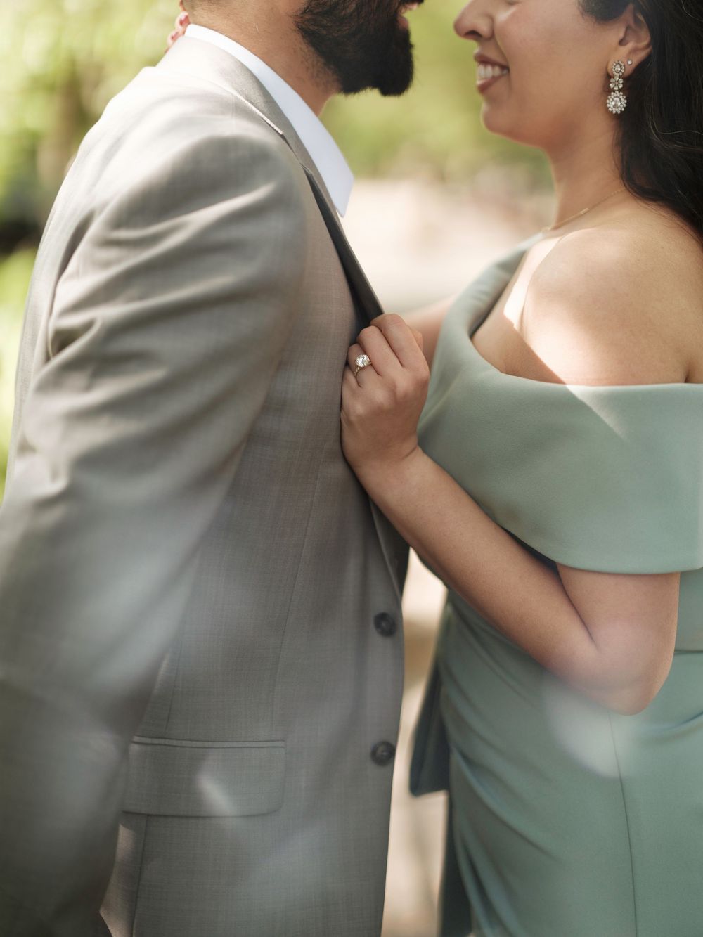 A couple in formal attire share an intimate moment, with her in a sage green dress and him in a light gray suit.