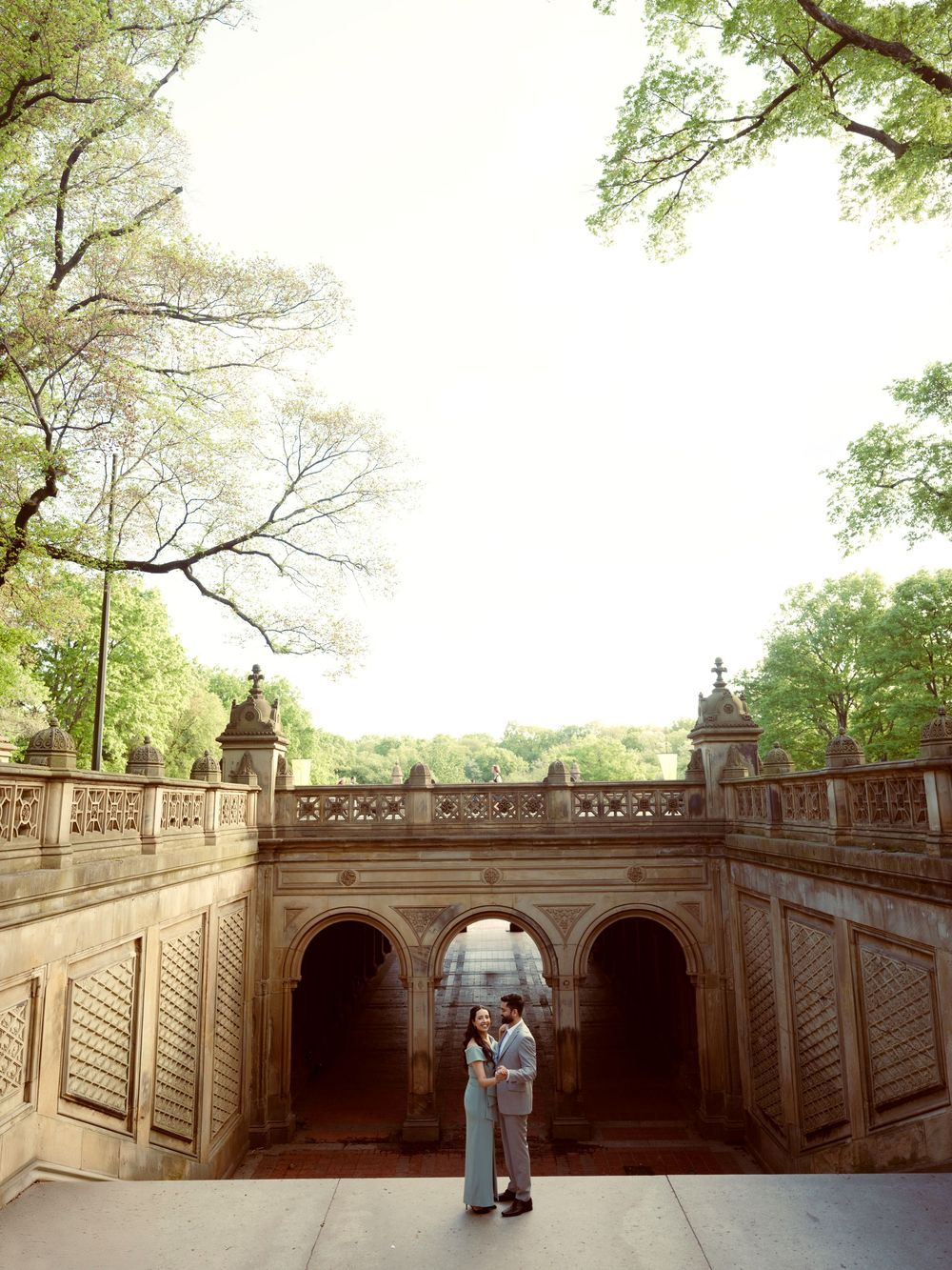 Romantic scene at Central Park's iconic Bethesda Terrace underpass with stone arches and dappled sunlight through trees.
