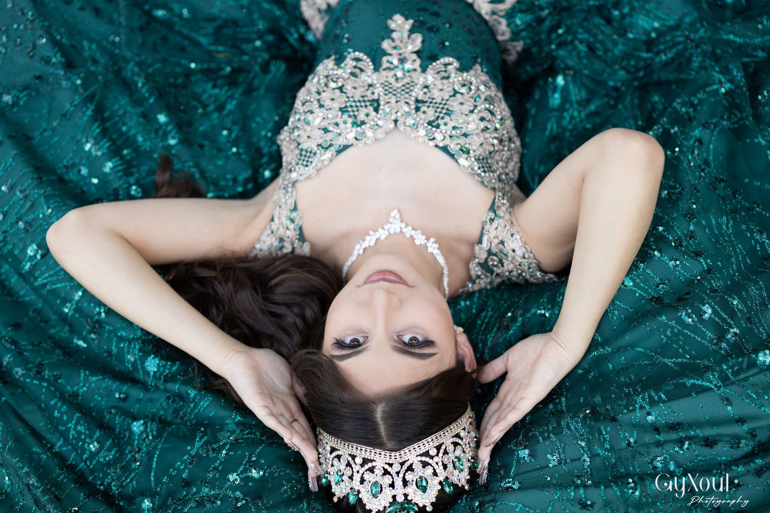 Aerial view of a person in an elegant teal green ballgown with silver tiara and jewelry laying on fabric.