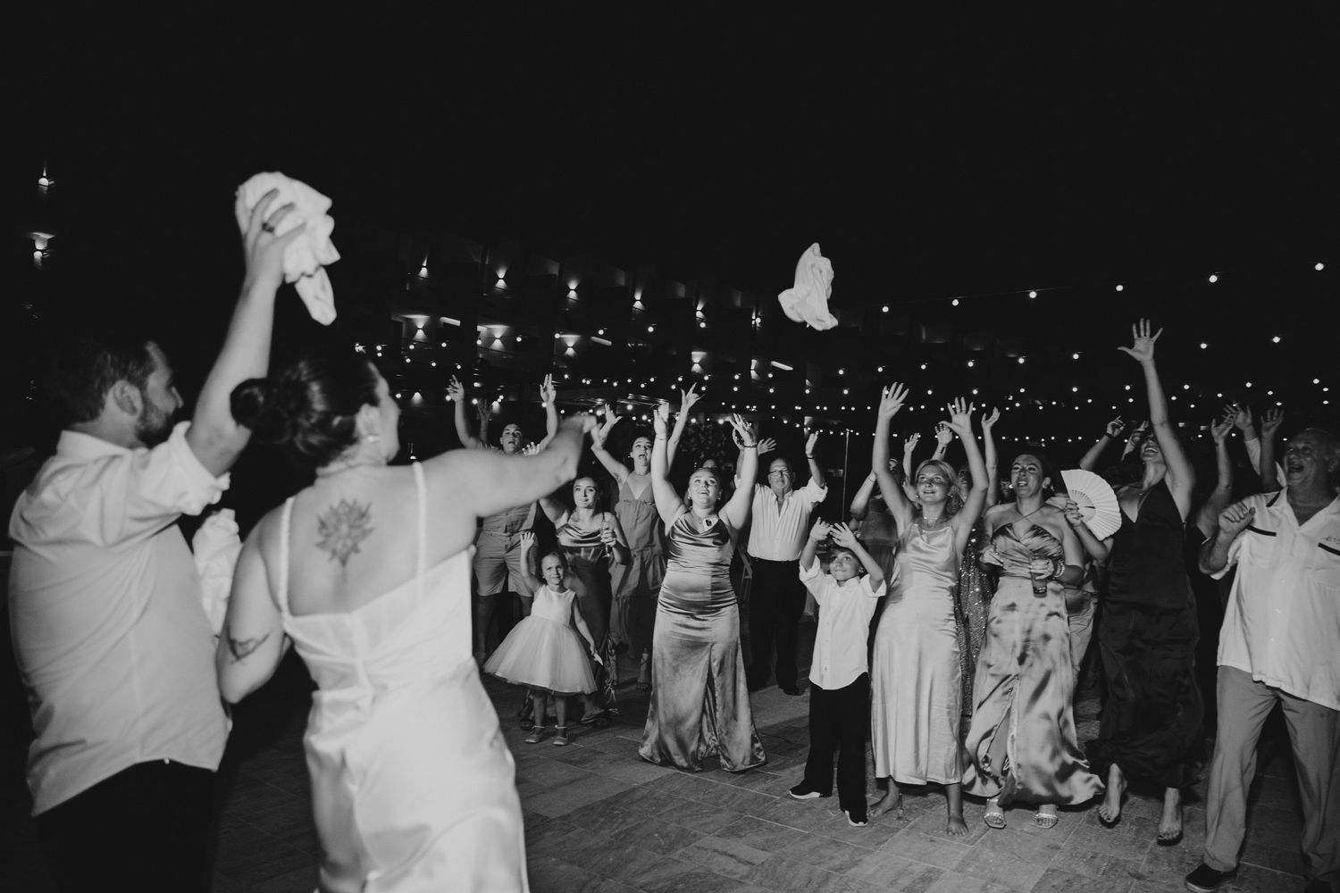 Black and white photo of wedding guests dancing and celebrating on an outdoor dance floor.