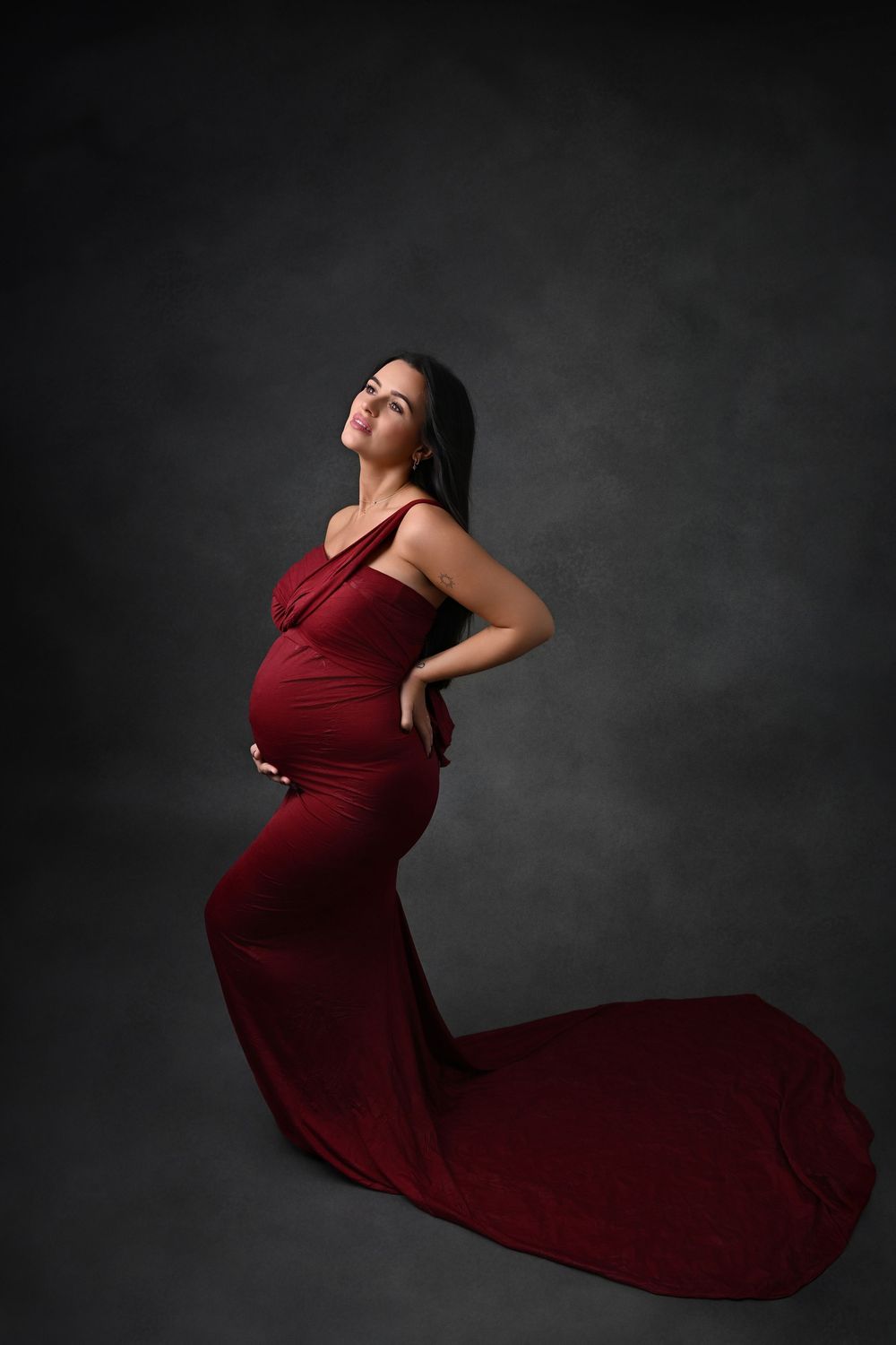 maternity portrait in burgundy gown against dark background.