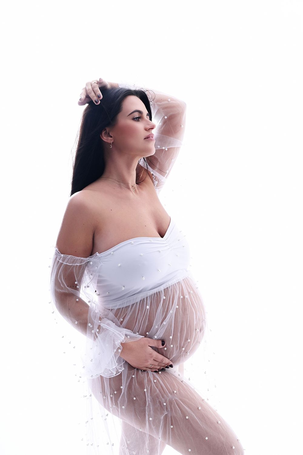 Ethereal maternity portrait in flowing white sheer fabric against light background.
