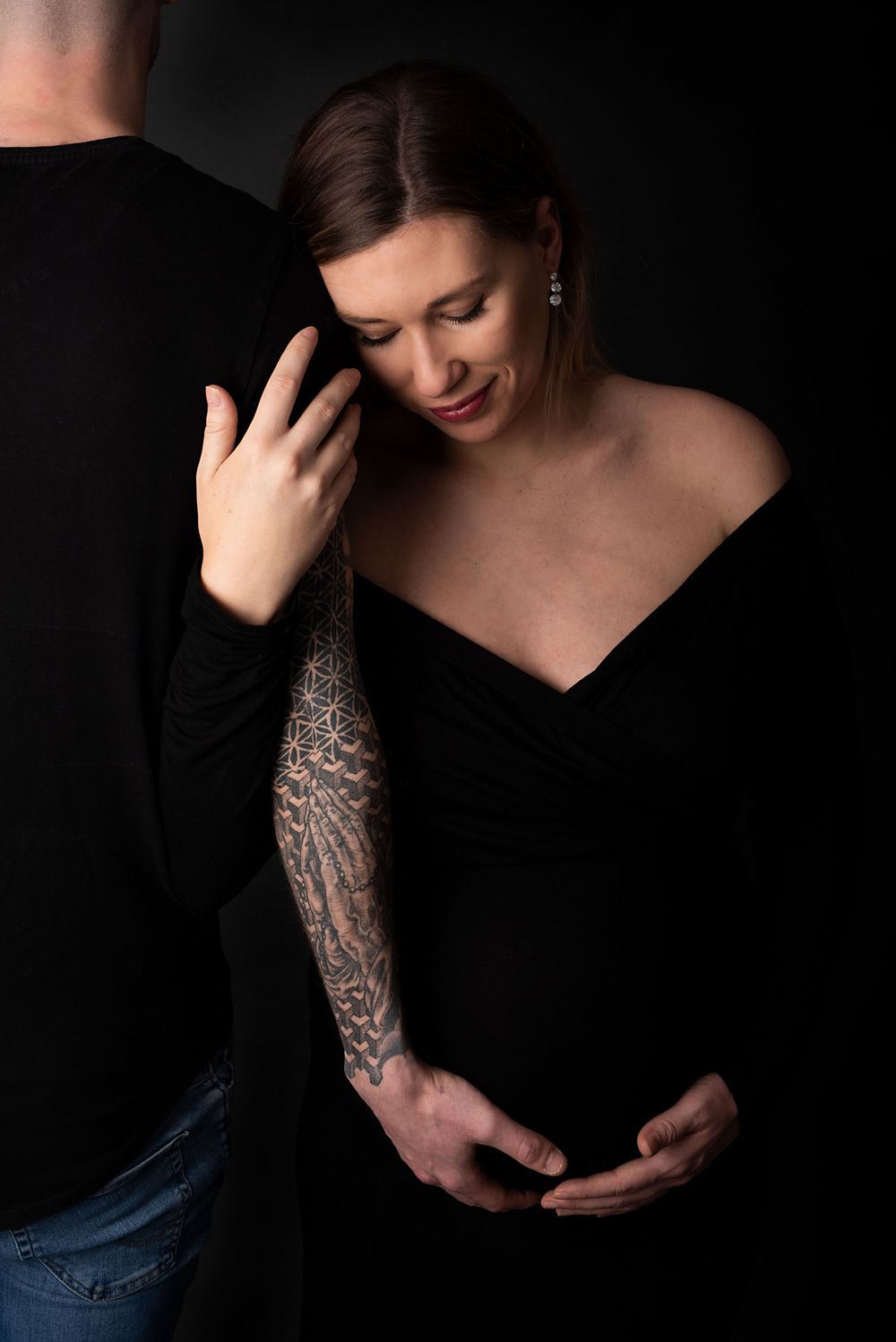 maternity portraits showing tattooed arm and black top against dark background.
