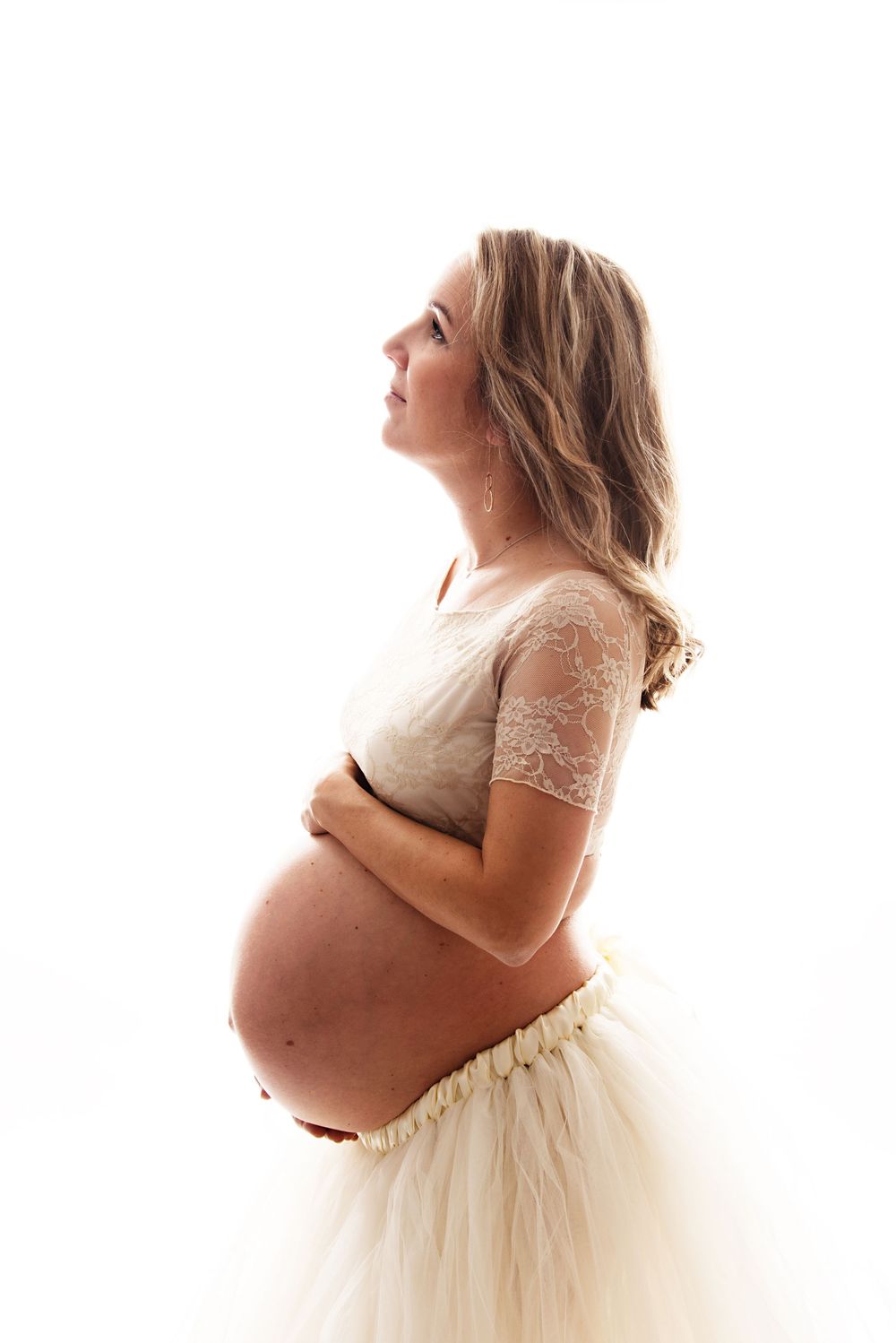 Romantic maternity portraits in cream lace top and tulle skirt with backlighting.