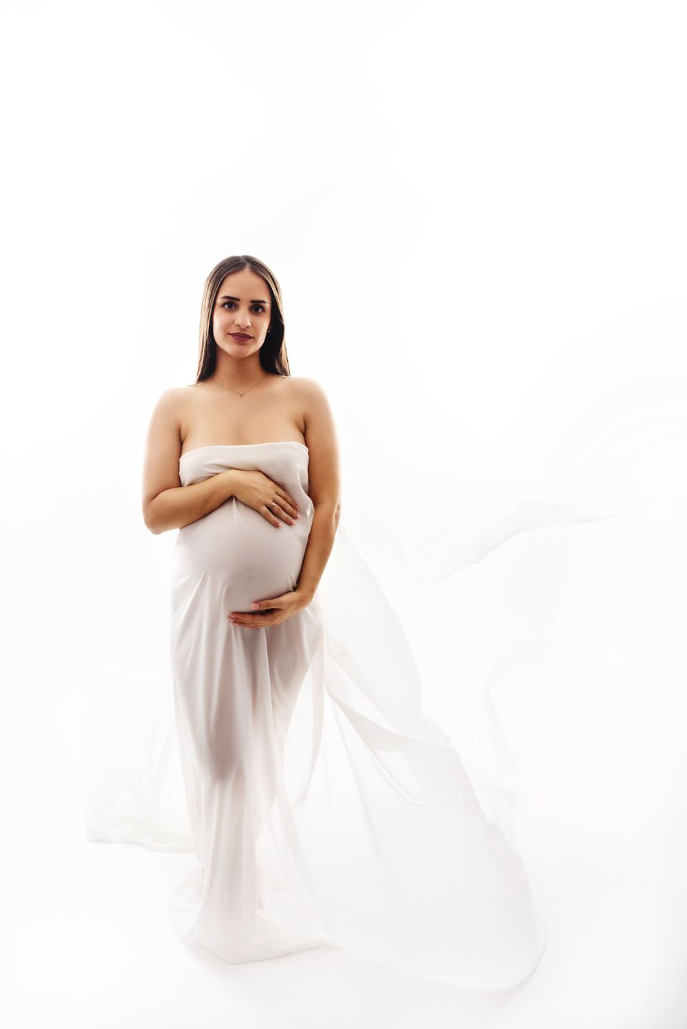 Ethereal maternity portraits with flowing white fabric against bright background.
