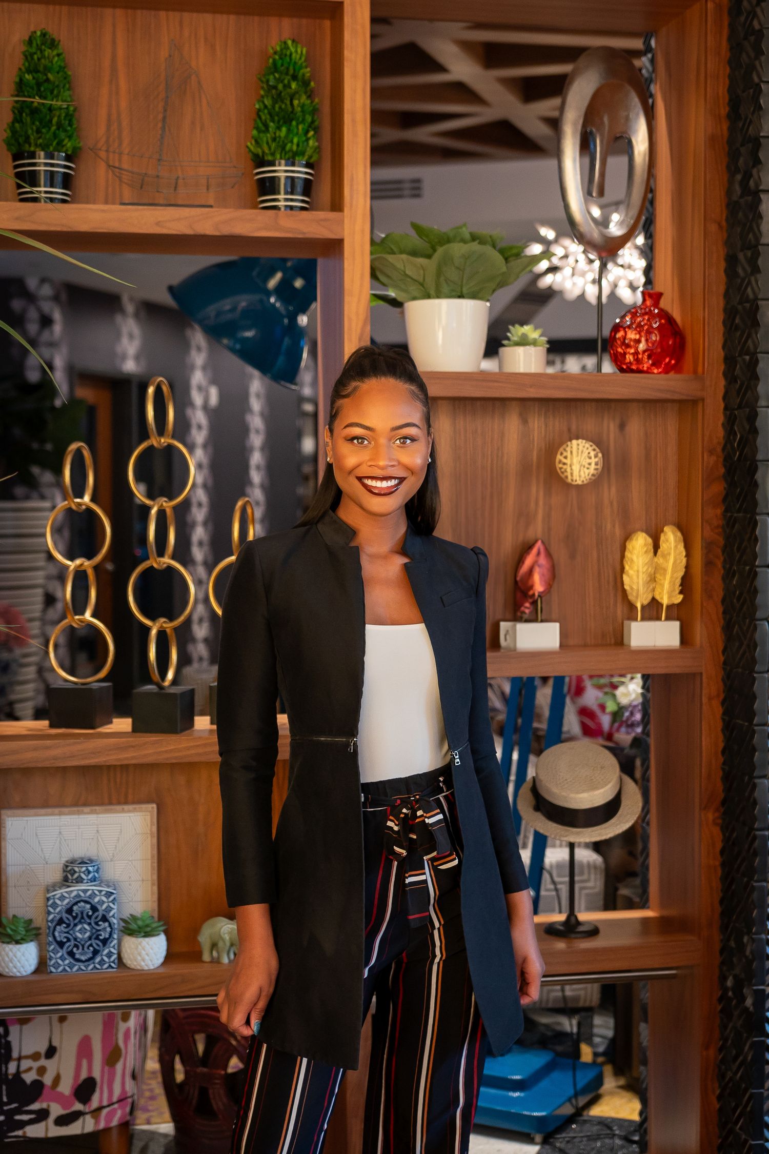 Stylish professional stands in front of wooden shelving displaying home decor items and fashion accessories.