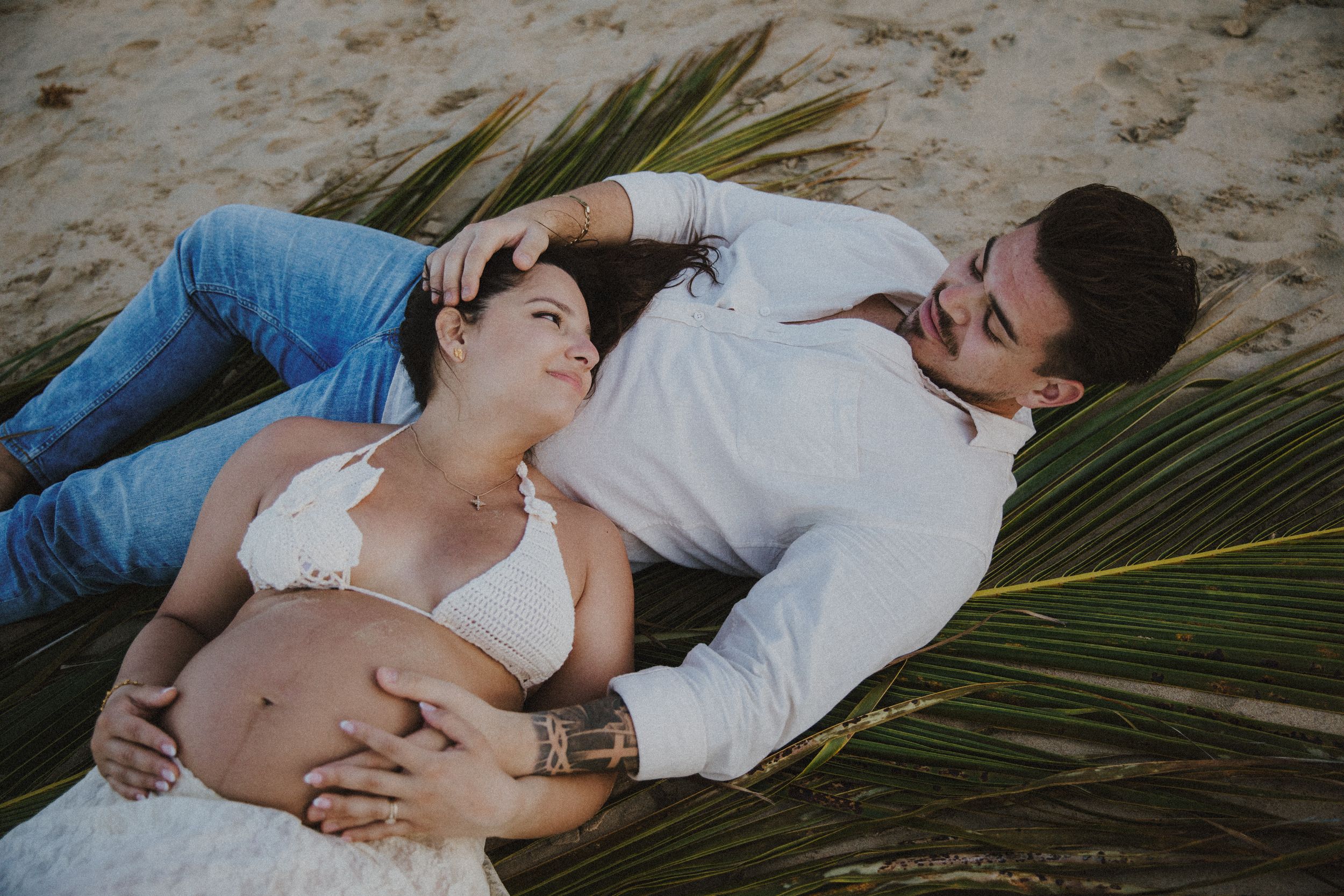 A romantic couple reclines on palm leaves on a tropical beach.