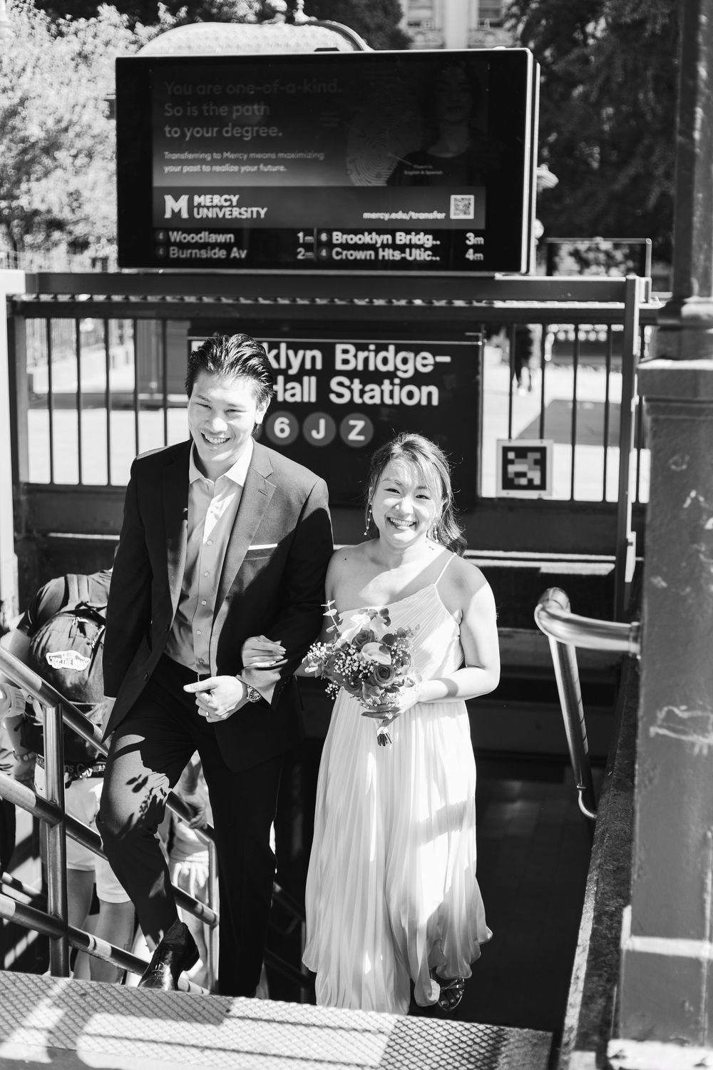 A happy couple and their loved ones share joyful moments near a subway station entrance on their wedding day.