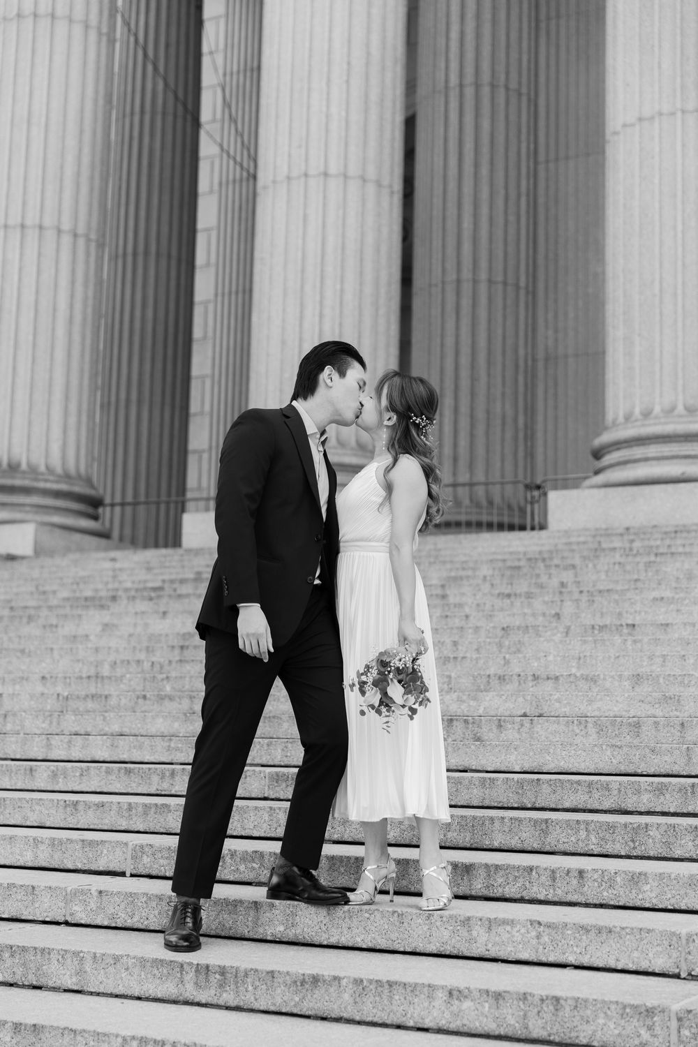 A couple climbing marble steps together in front of classical building columns.