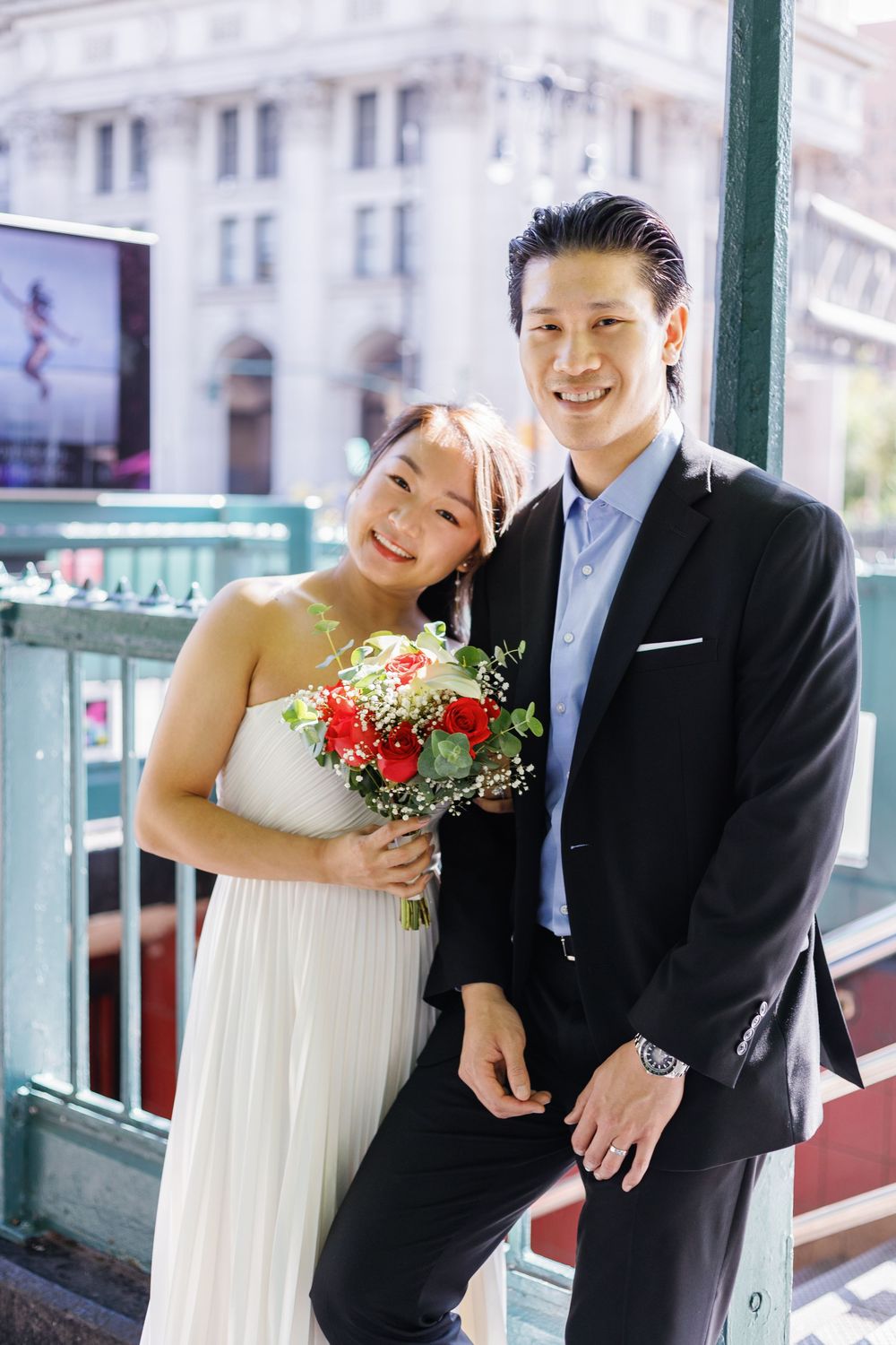 Newlywed couple shares joyful moments in their wedding attire while posing along a bright outdoor balcony area.