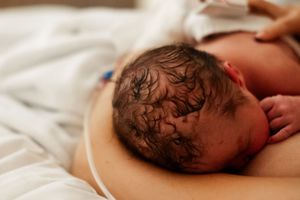 Close-up series showing newborn baby with dark hair resting on white hospital bedding.