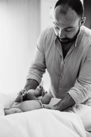 Healthcare provider in light colored shirt examining newborn baby on white bedding.