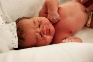 Side view sequence of newborn baby resting peacefully on white hospital sheets.