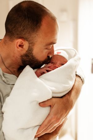 Parent in white shirt holding and bonding with swaddled newborn baby.