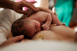 Gentle hands supporting newborn baby during first moments after birth.