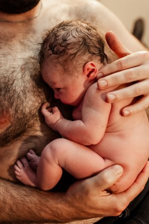 Intimate skin-to-skin contact between newborn and parent in warm lighting.