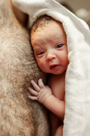 Newborn wrapped in white blanket during skin-to-skin contact.