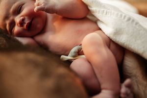 Newborn baby stretching during skin-to-skin contact under white blanket.