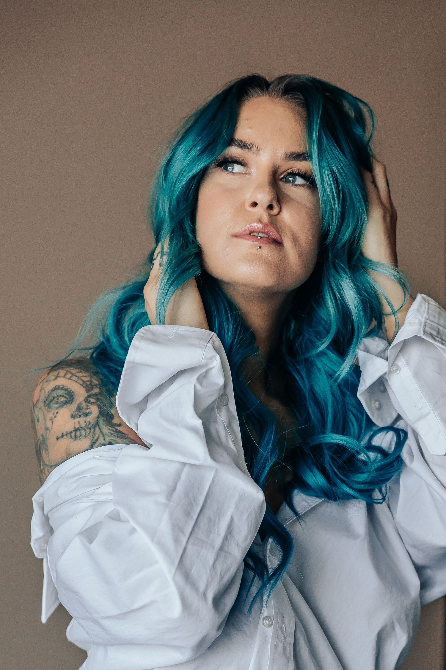 Person with vibrant blue hair and tattoos poses in white shirt against neutral background, in Red Deer, Alberta.