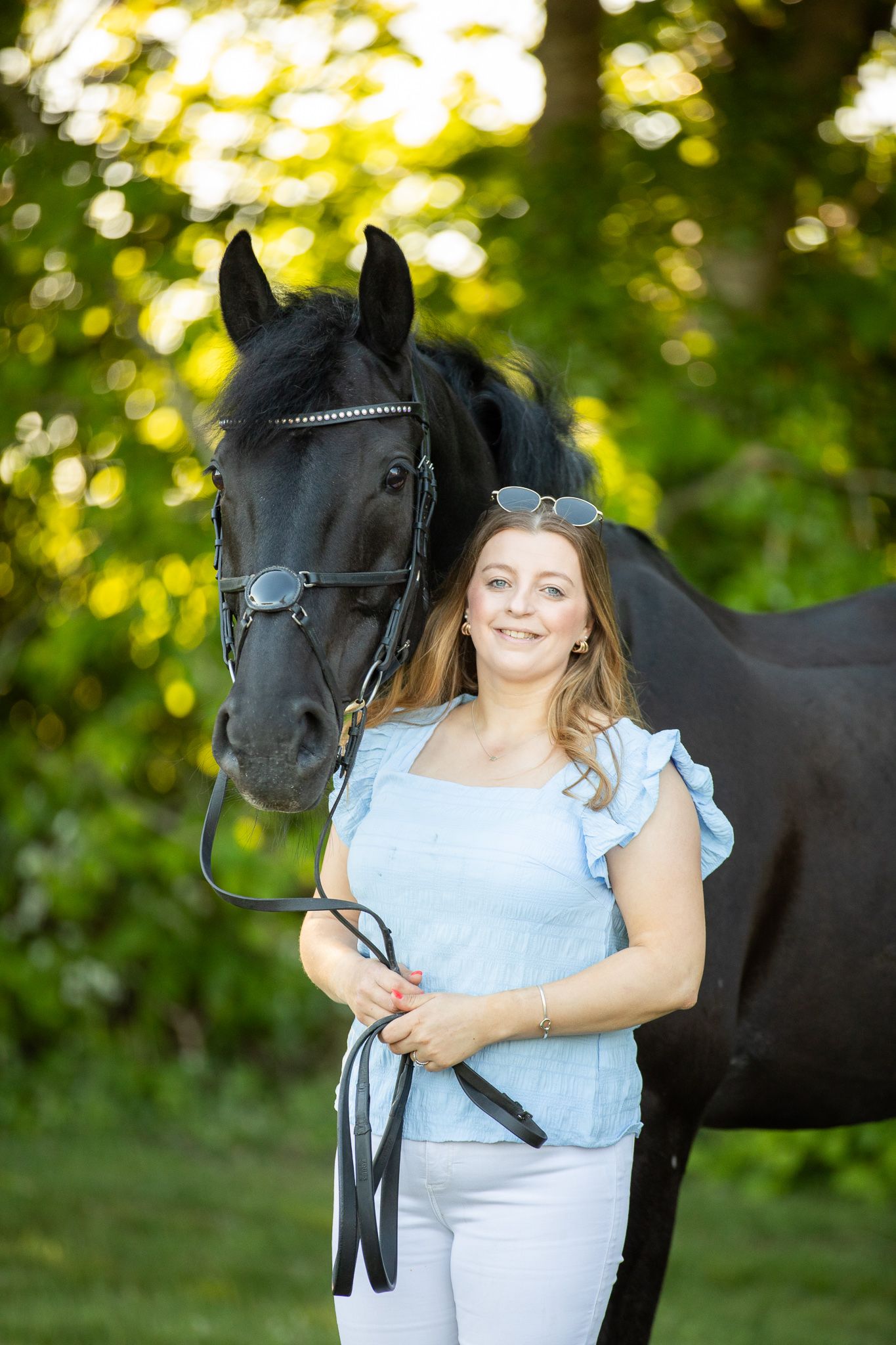Young girl in denim overalls embraces a palomino horse in a sun-dappled forest setting.