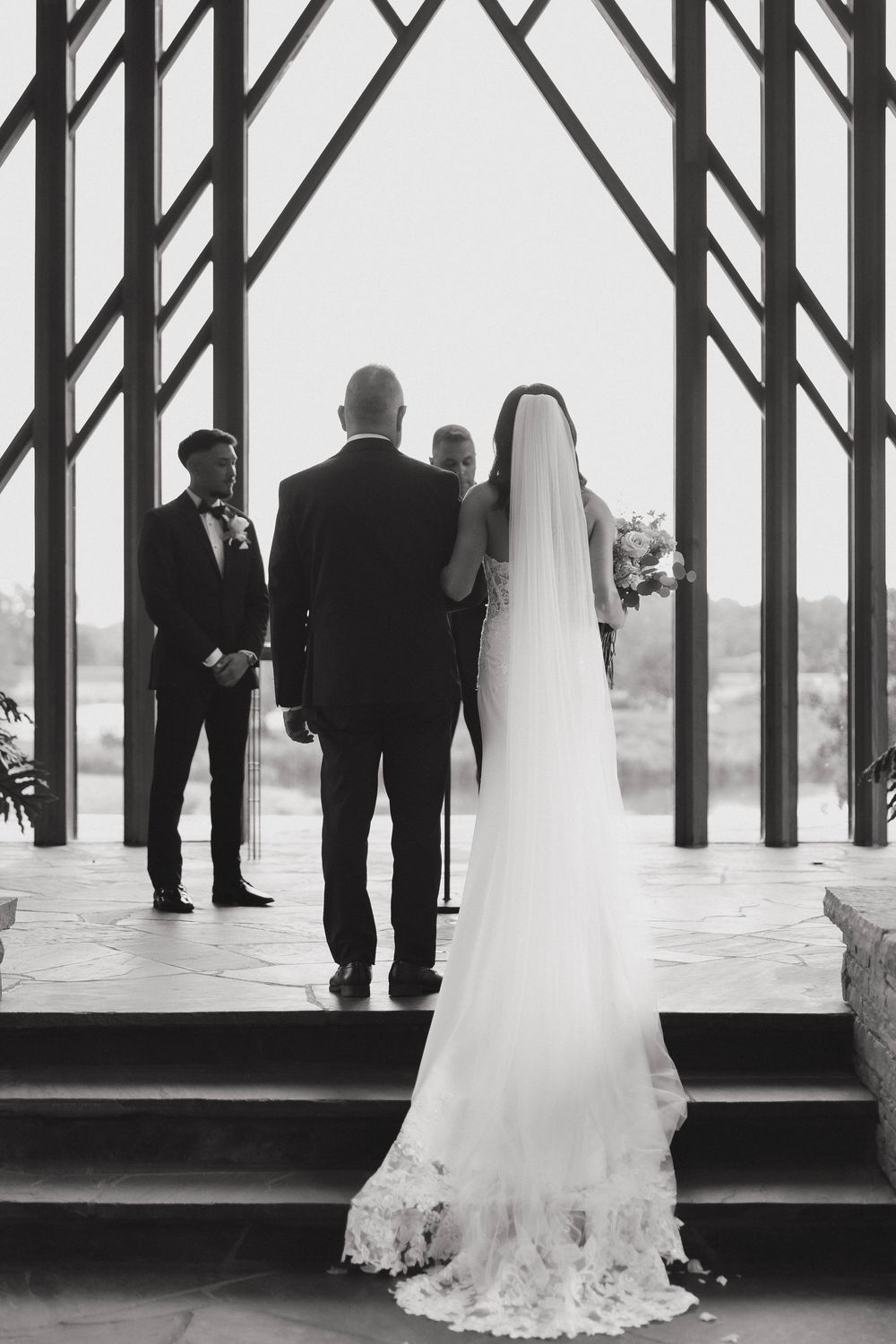 Black and white wedding ceremony photo showing silhouettes against dramatic architectural beams.