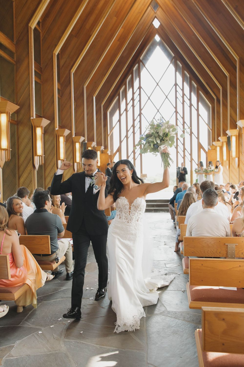 Guests celebrate with joy in a beautiful wooden chapel with vaulted ceilings and natural light streaming through windows.