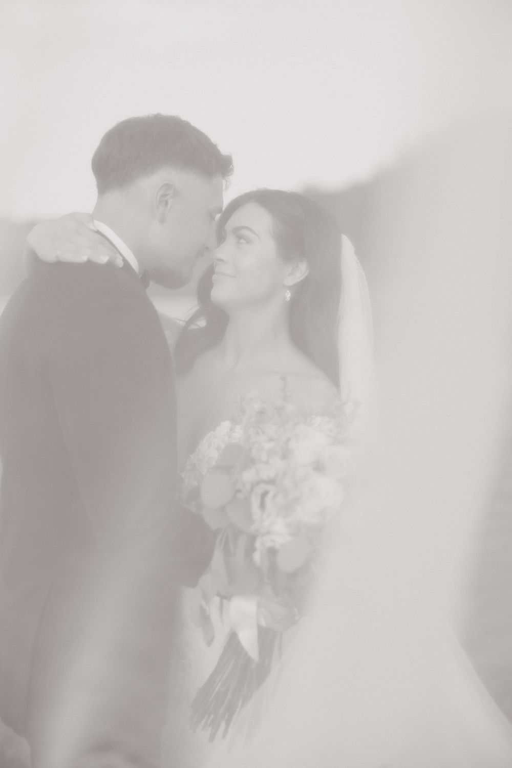 Soft focus vintage black and white photograph of two people sharing an intimate wedding moment with a bouquet.