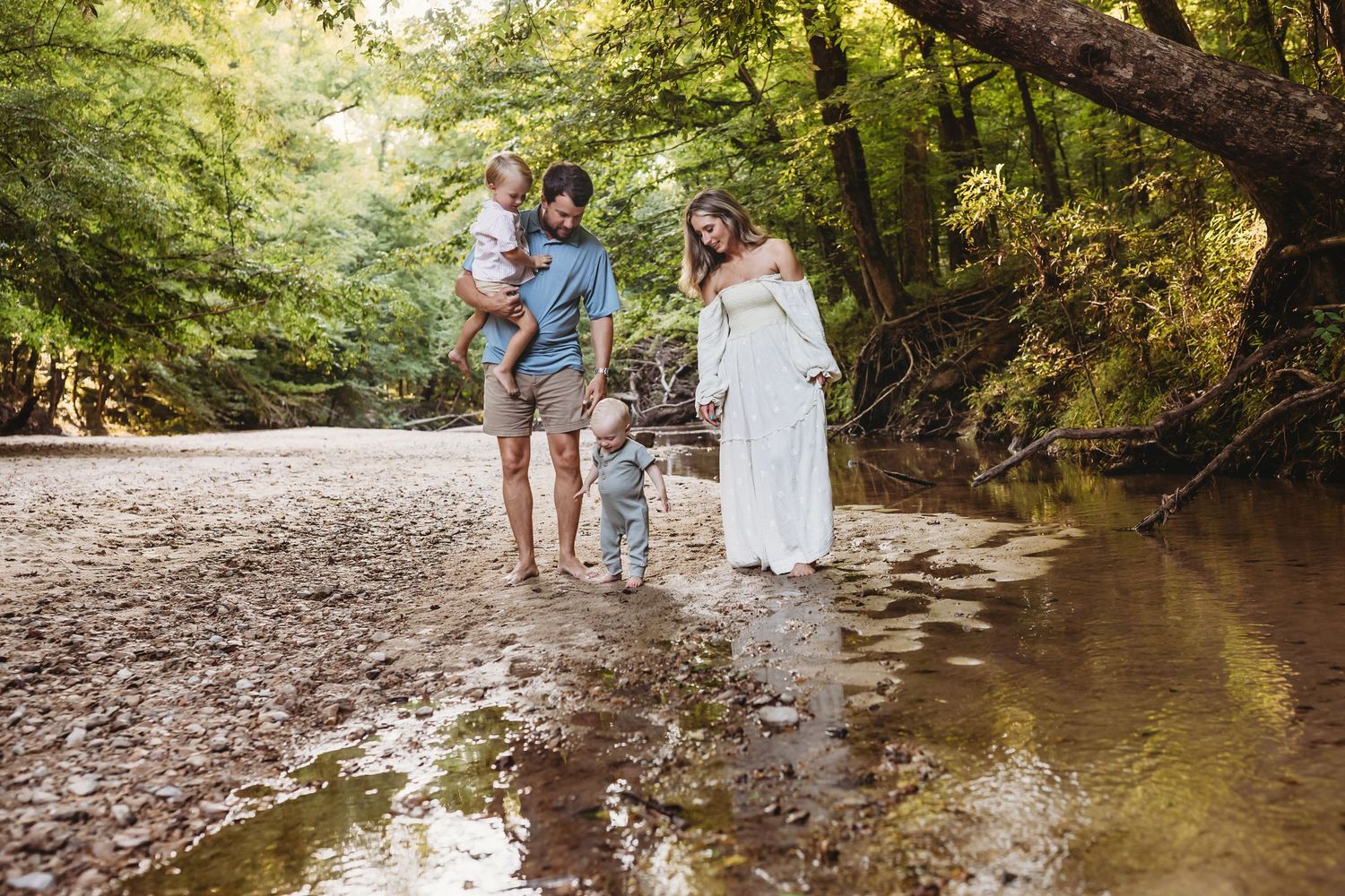 A family poses in a sunlit creek bed surrounded by lush forest greenery during a nature photo session.
