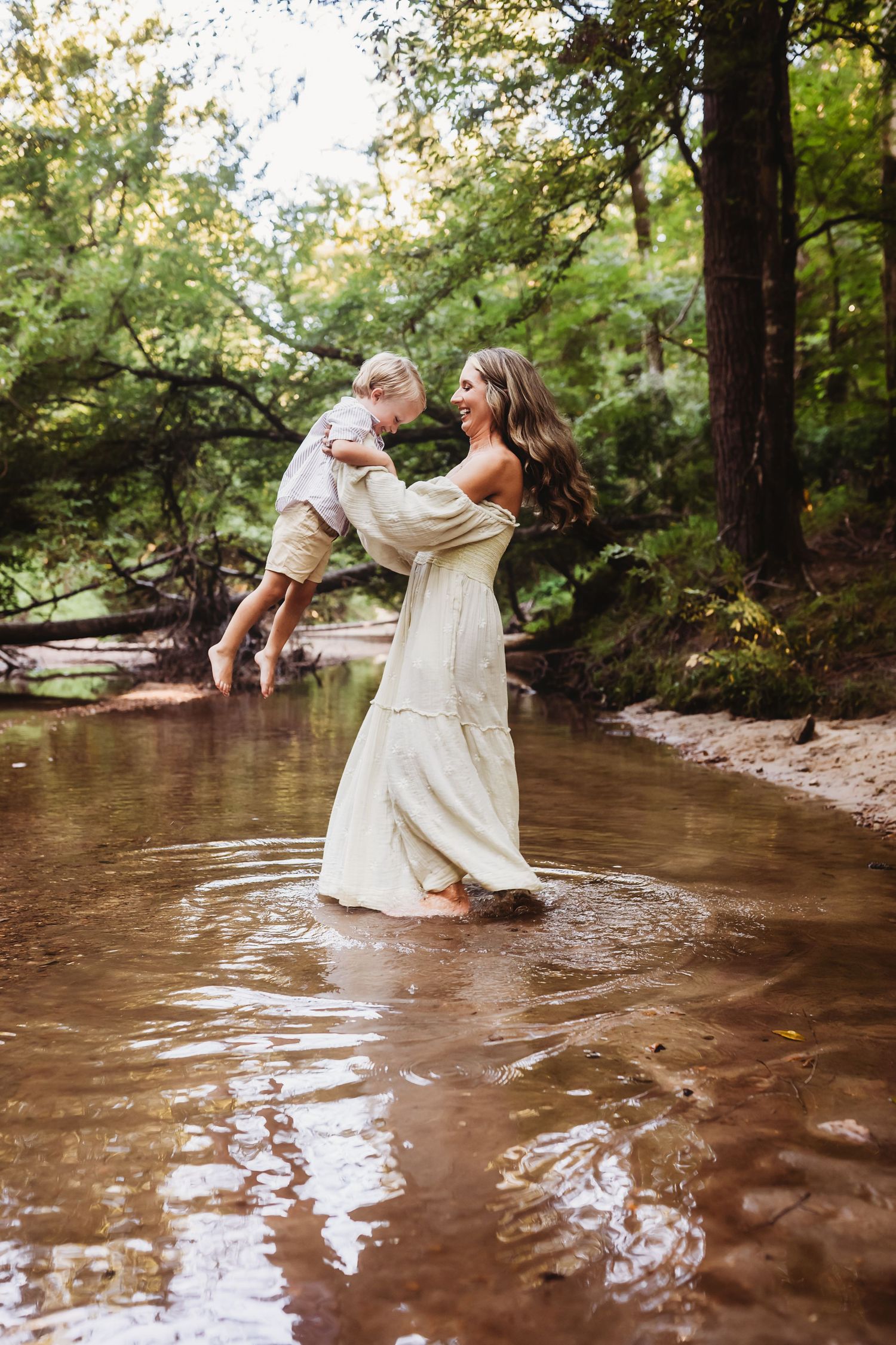 A newlywed couple playfully splashes and dances in a rustic creek surrounded by lush green forest.
