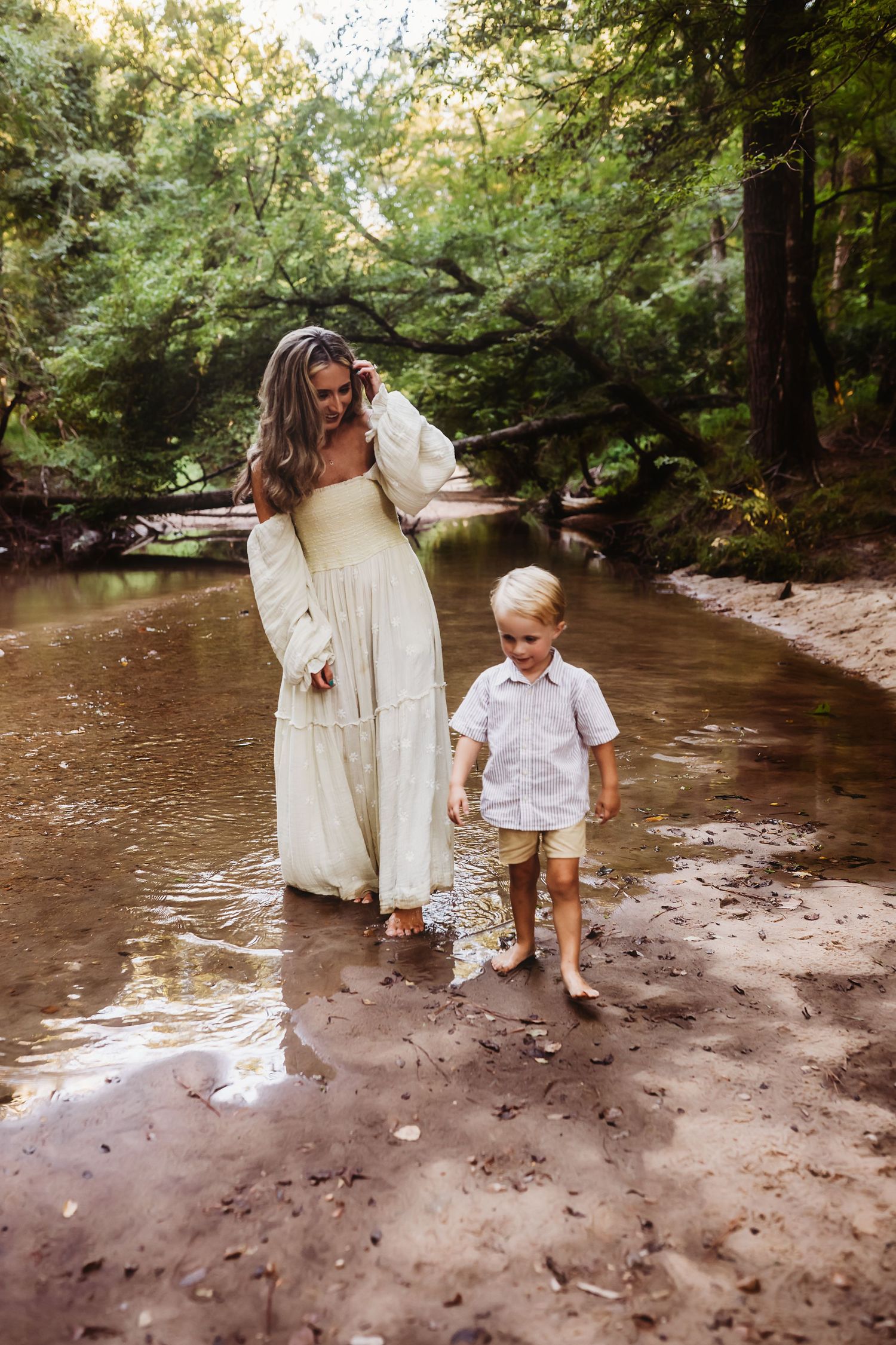 Two people enjoying a peaceful moment together by a creek in a lush forest setting at golden hour.