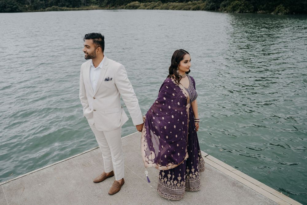A couple in white and purple attire sits peacefully by the water's edge, creating a romantic lakeside moment.