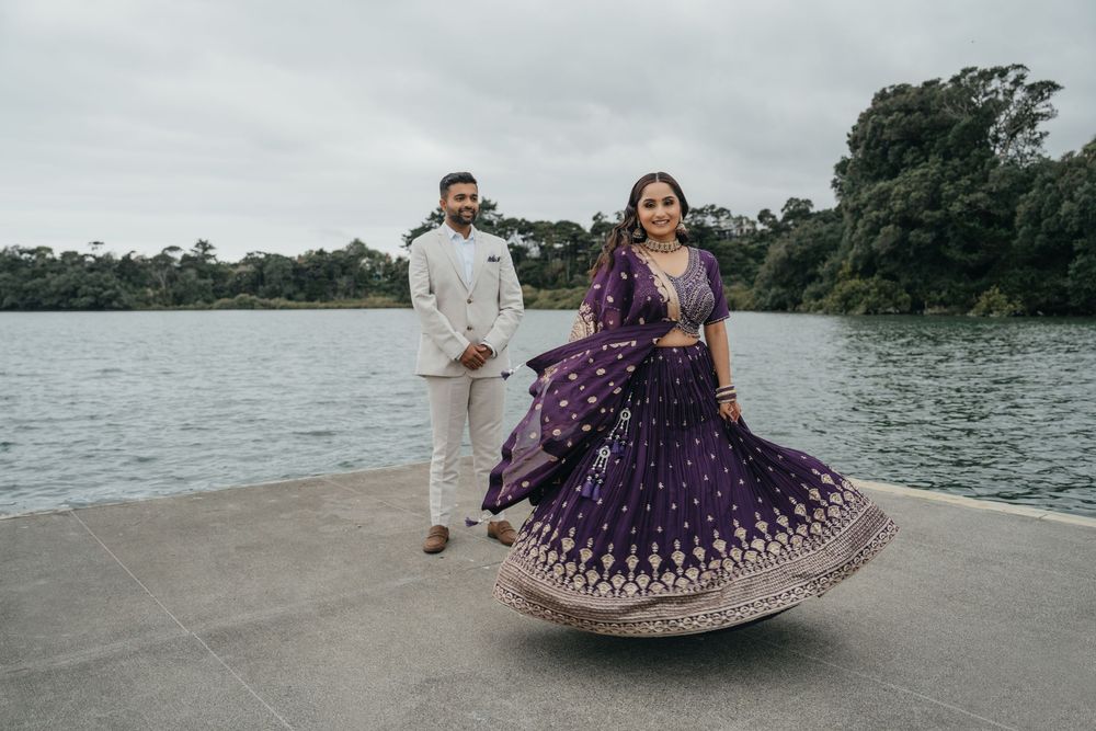 Two people in traditional Indian wedding attire pose along a beach shoreline during golden hour.