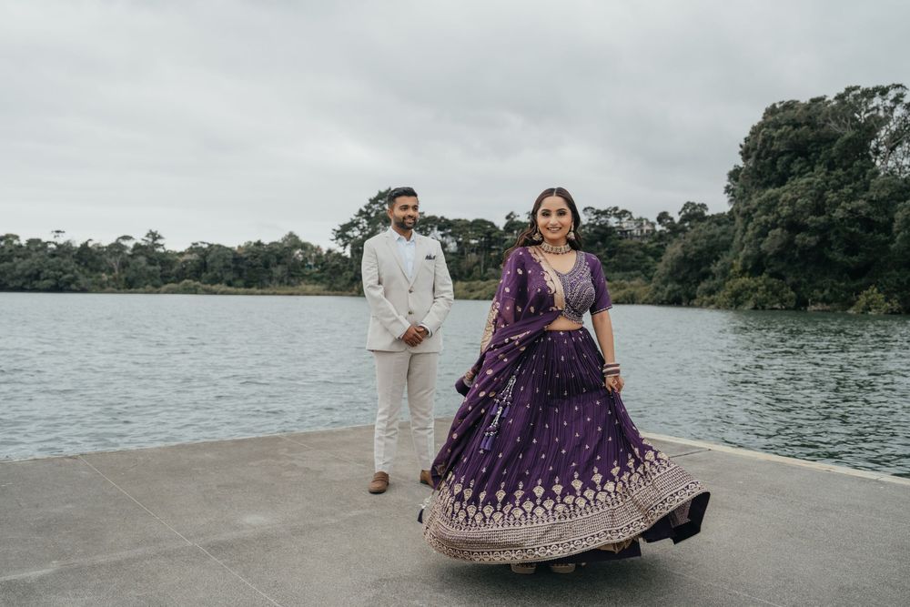 A couple dressed in formal Indian attire poses together near a scenic lakeside during their engagement photoshoot.