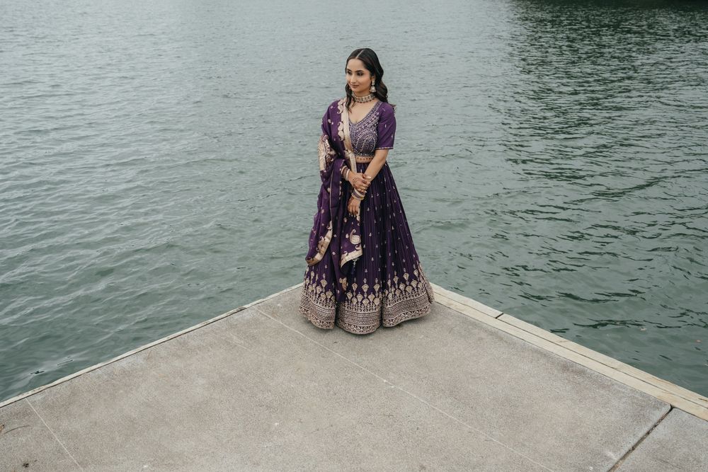 A person in a beautiful blue dress sits gracefully on a concrete pier overlooking the water.