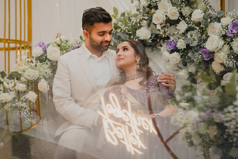Wedding couple stands together in an elegant white floral archway with soft lighting and decorative accents.