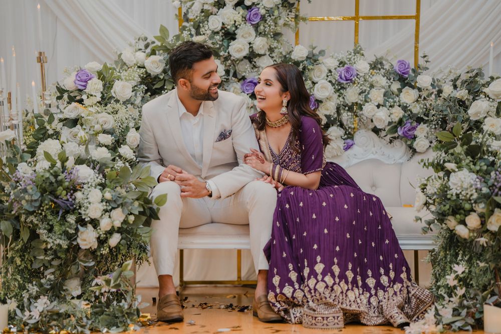 A joyous couple shares intimate moments at a wedding reception decorated with white floral installations and golden accents.