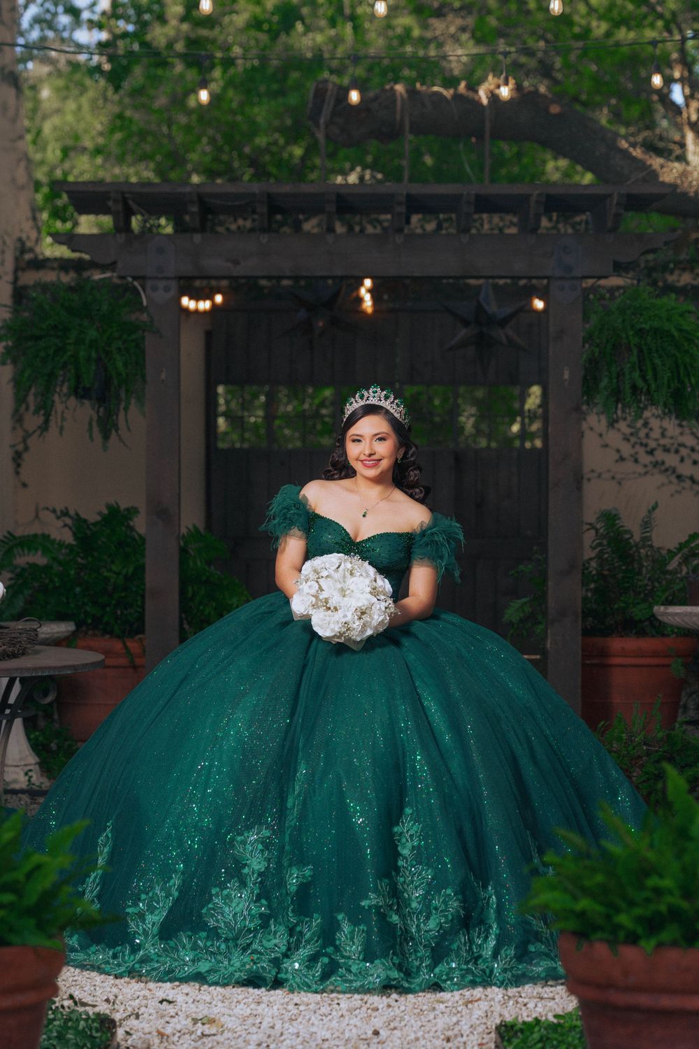 A stunning emerald green quinceañera ball gown photographed in a garden setting with string lights.