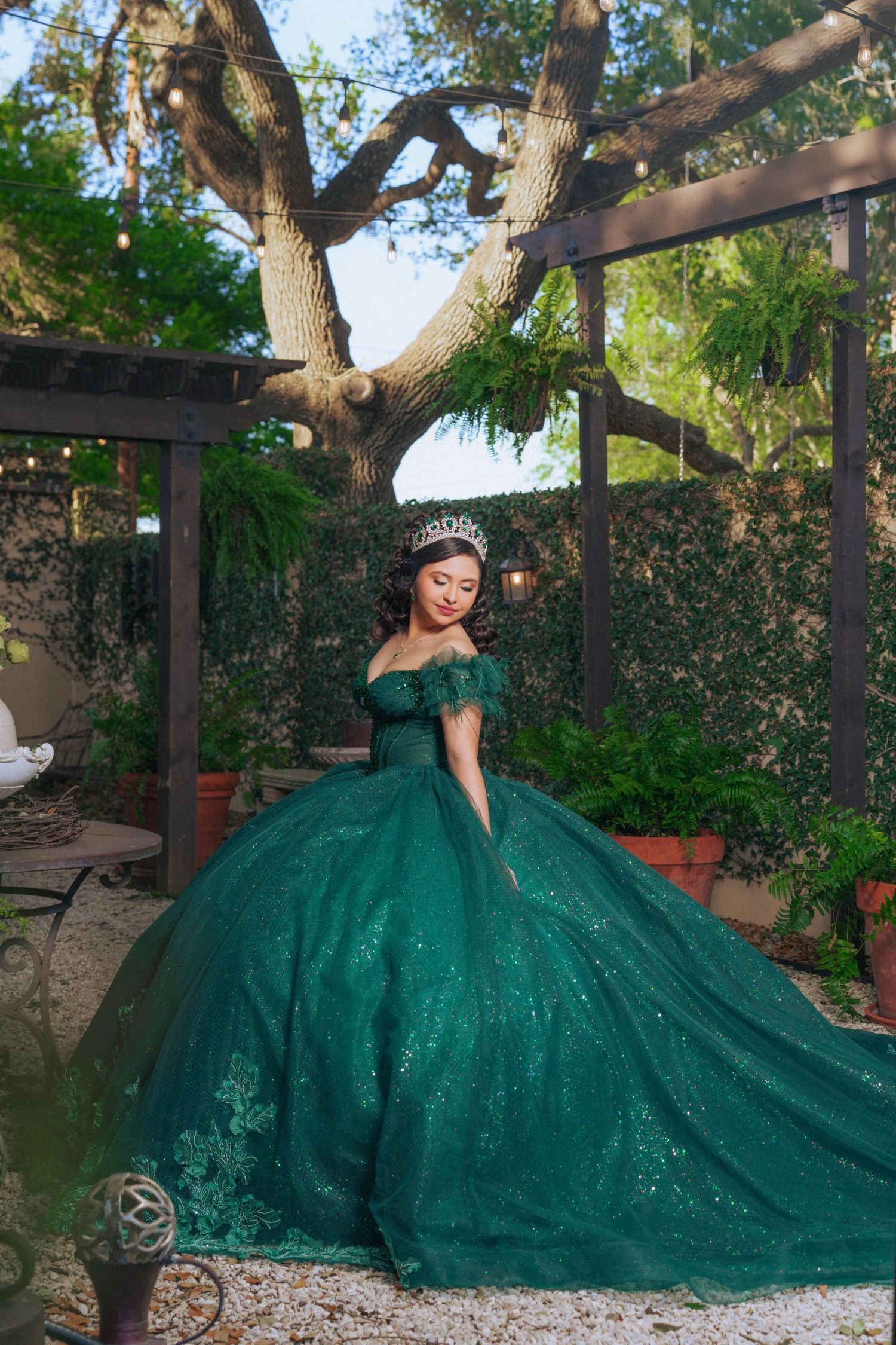 An elaborate emerald green ball gown sparkles under a garden pergola with twinkling lights.