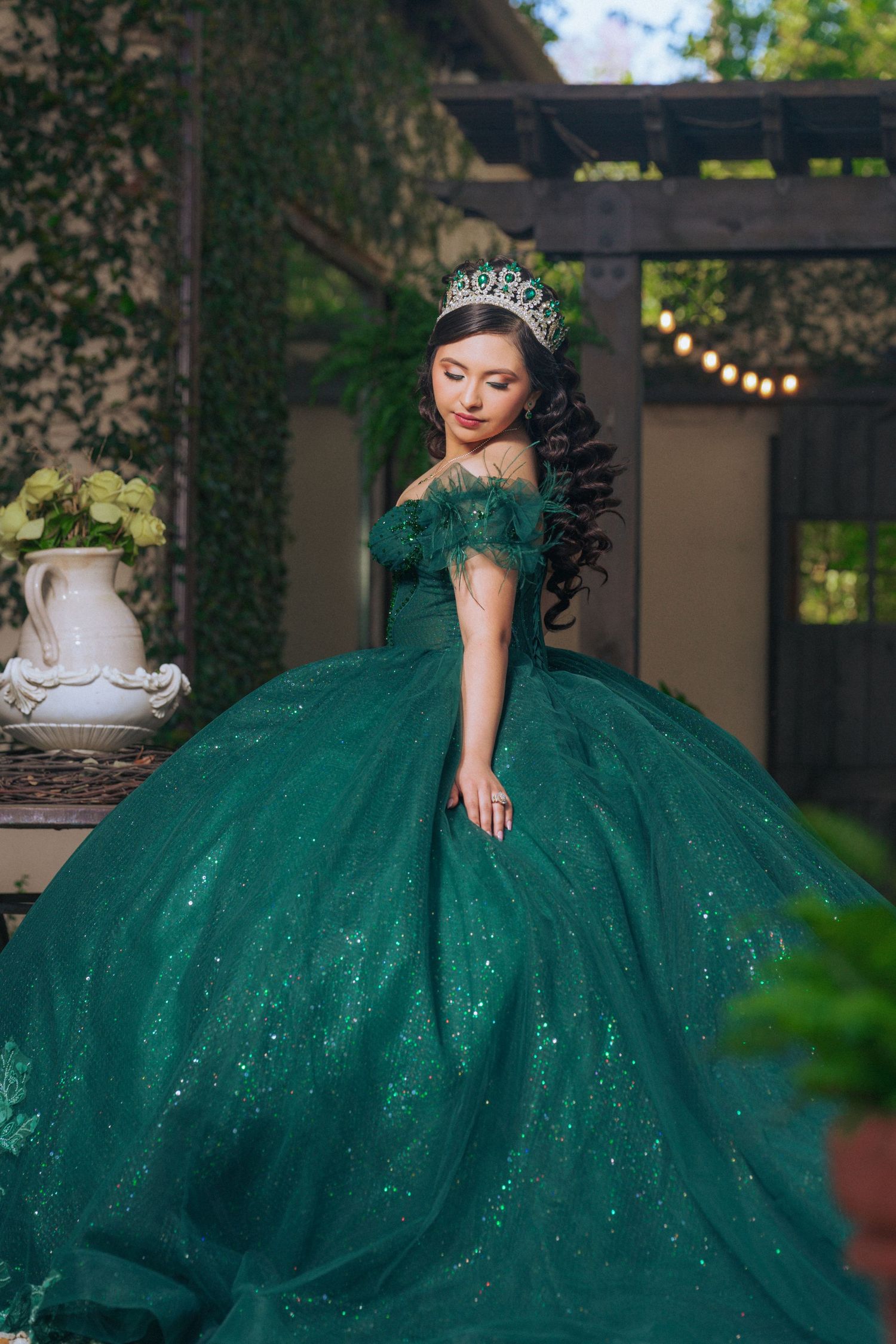 A sparkling emerald green ball gown with off-shoulder design photographed in an outdoor garden setting.