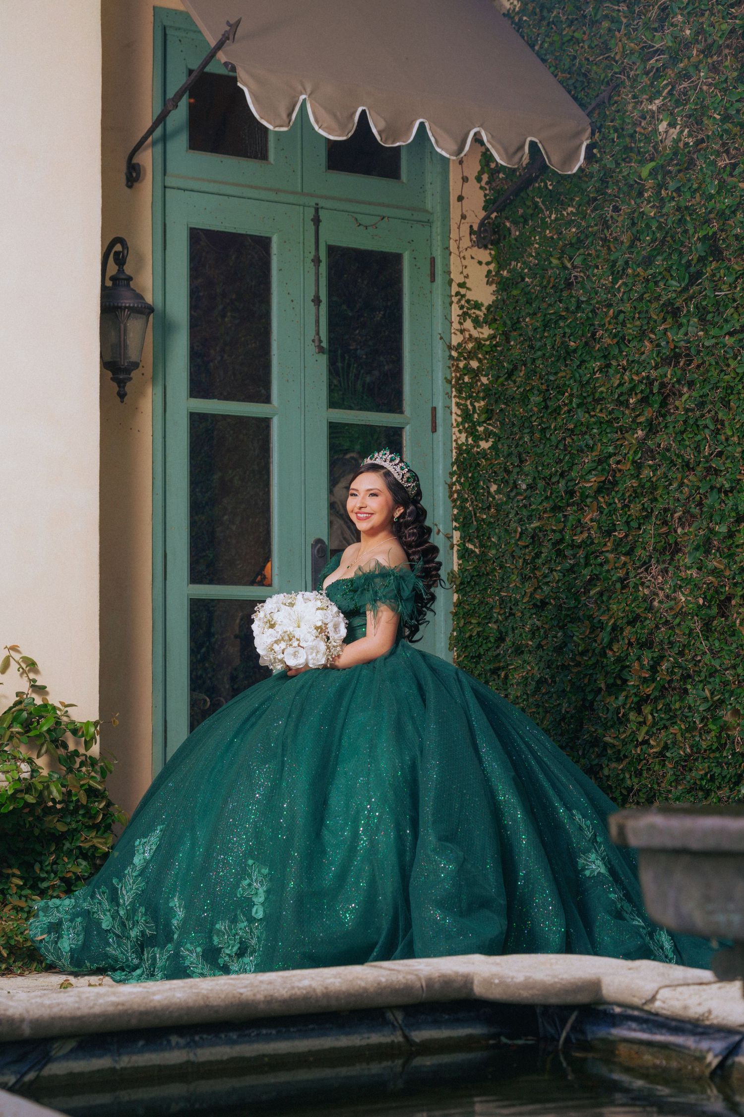 A stunning emerald ball gown photographed in front of vintage green doors with a white bouquet.