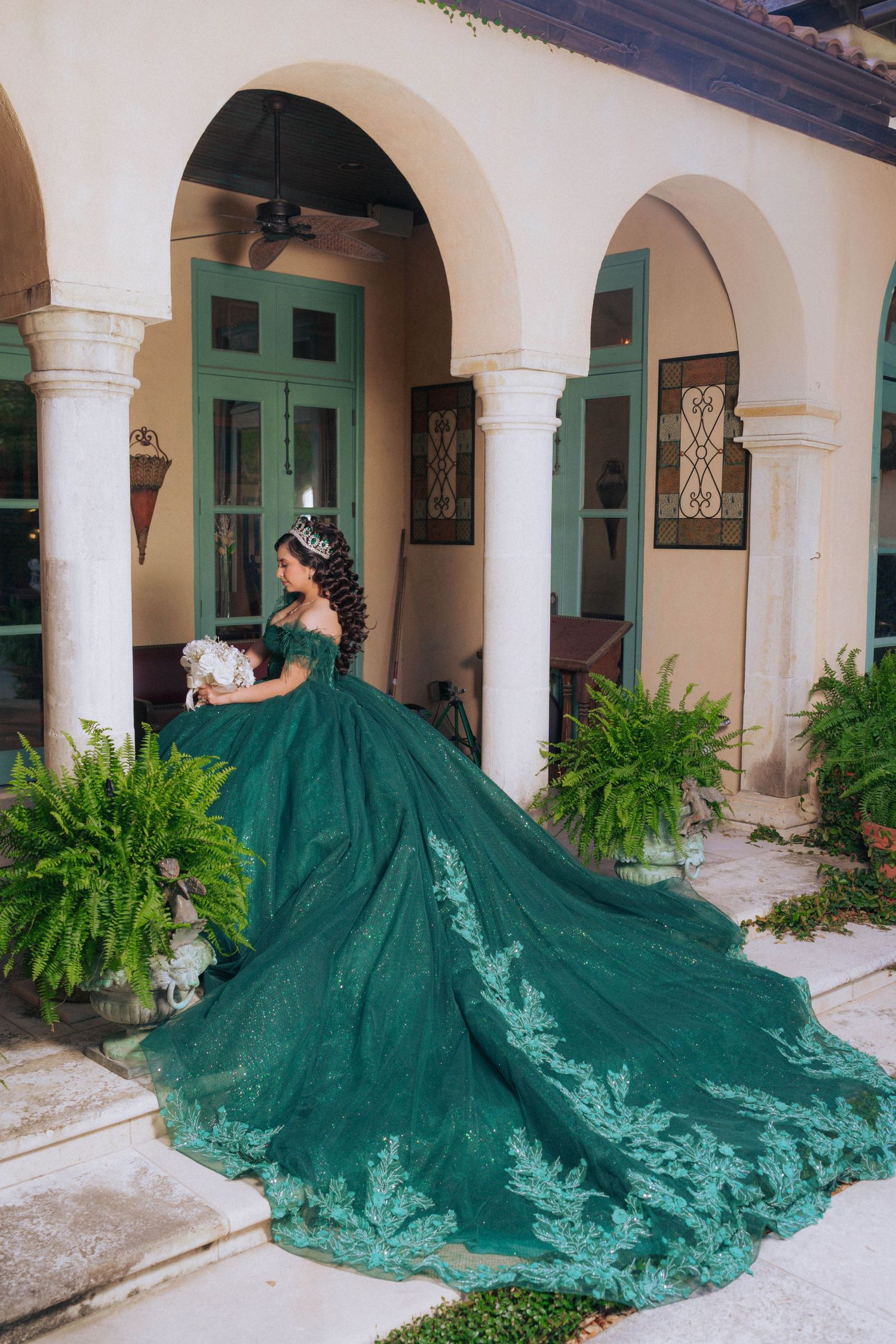 An elaborate emerald green ball gown with long train photographed in an elegant courtyard with arches.