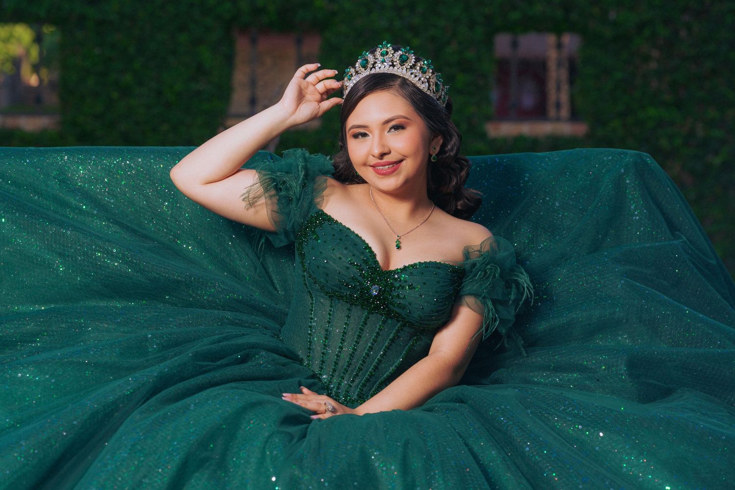 A sparkling emerald green ball gown with tiara photographed against a garden backdrop.
