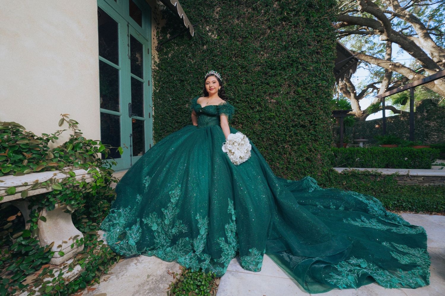 Stunning emerald green ballgown photographed against Spanish colonial architecture with ivy-covered walls.
