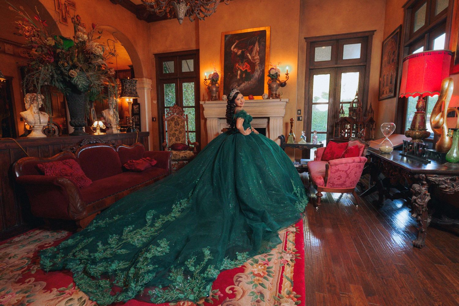 Luxurious emerald ballgown displayed in warmly lit Spanish colonial interior with wooden beams.