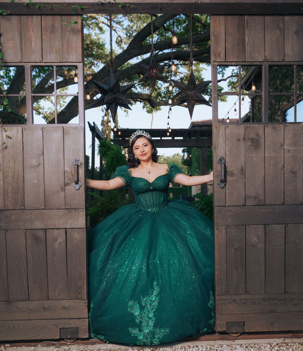 Emerald quinceañera dress showcased against rustic wooden gates in outdoor setting.